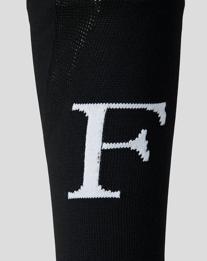 Close-up of white Feyenoord F logo on black sock leg.