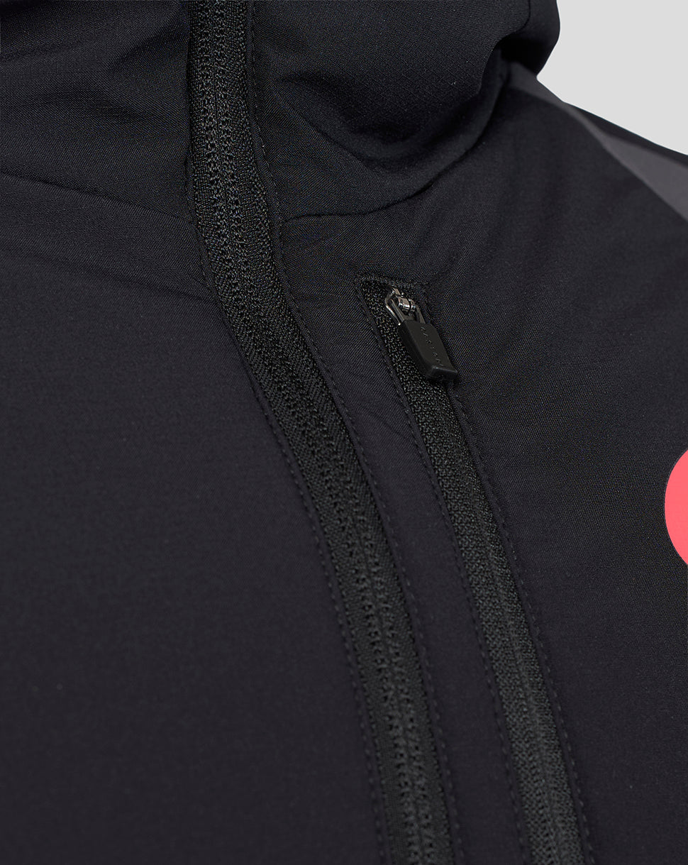 Close-up of a black hooded jacket with a black zipper, showing the fabric texture and a partial bright pink circular logo on the side.
