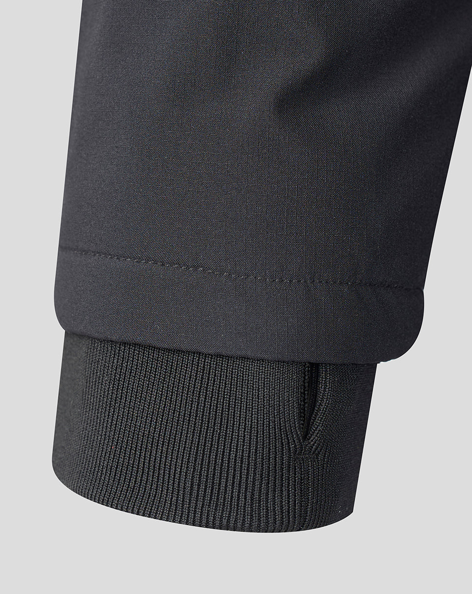 Close-up detail of a dark charcoal gray garment sleeve showing a ribbed knit cuff and stitched hem against a light gray background.