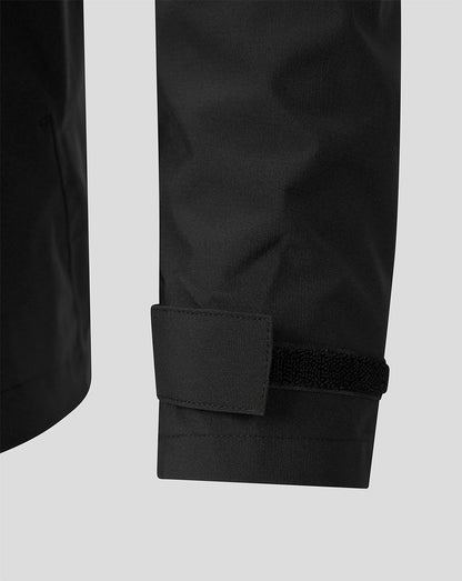 Close-up of a black garment sleeve with a cuff tab and hook-and-loop strap closure, shown against a light gray background.