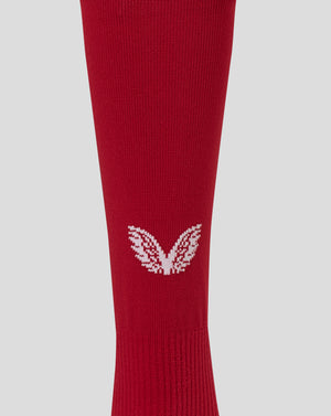 A close-up of a red ribbed knit sock featuring a white embroidered wing logo near the lower calf, set against a solid light gray background.