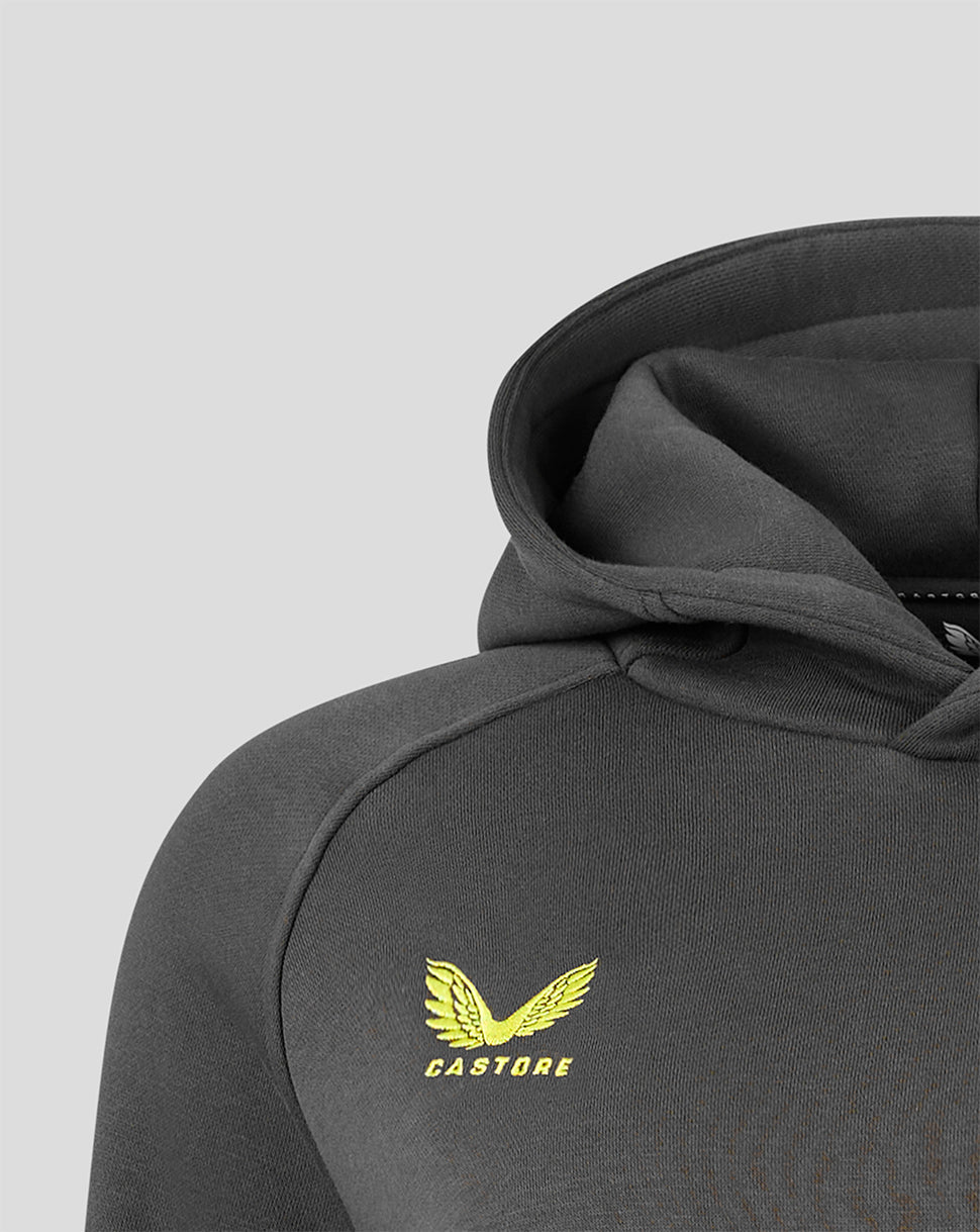 Close-up of a dark gray hooded sweatshirt showing the shoulder, sleeve, and hood, with a yellow Castore wing logo printed on the chest against a light gray background.