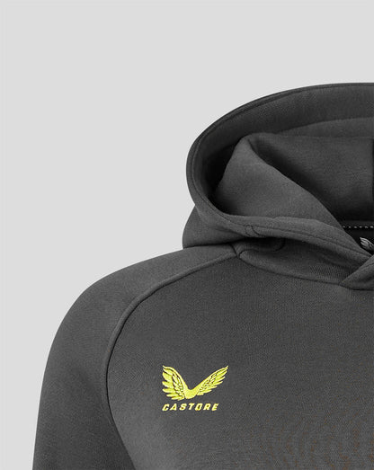 Close-up of a dark gray hooded sweatshirt showing the shoulder, sleeve, and hood, with a yellow Castore wing logo printed on the chest against a light gray background.