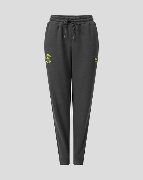 Dark gray jogger sweatpants with a drawstring waist, featuring a yellow-green circular crest on the left thigh and a matching logo on the right thigh, shown against a light gray background.