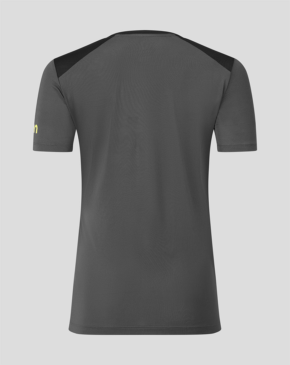 A dark gray athletic t-shirt shown from the back, featuring black shoulder panels and a small yellow logo on the left sleeve, set against a solid light gray background.