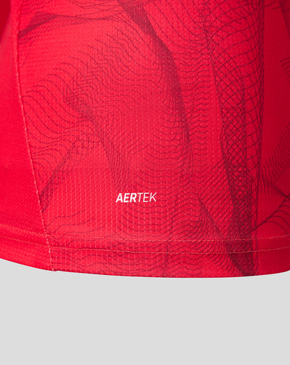 Close-up of a red athletic garment showing the AERTEK logo printed in white on the fabric, with a subtle dark wavy pattern over a bright red mesh-like surface.