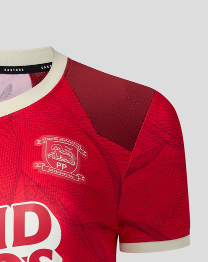 Close-up of a red sports jersey with a textured pattern, cream ribbed collar and cuffs, and a white crest on the chest.