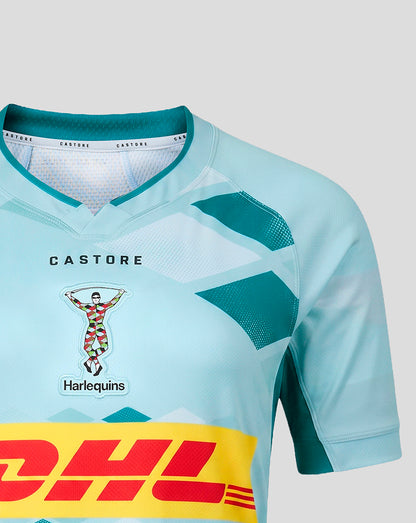 A close-up of a light blue and teal soccer jersey with a yellow DHL sponsor stripe across the bottom and a Harlequins team crest on the chest.