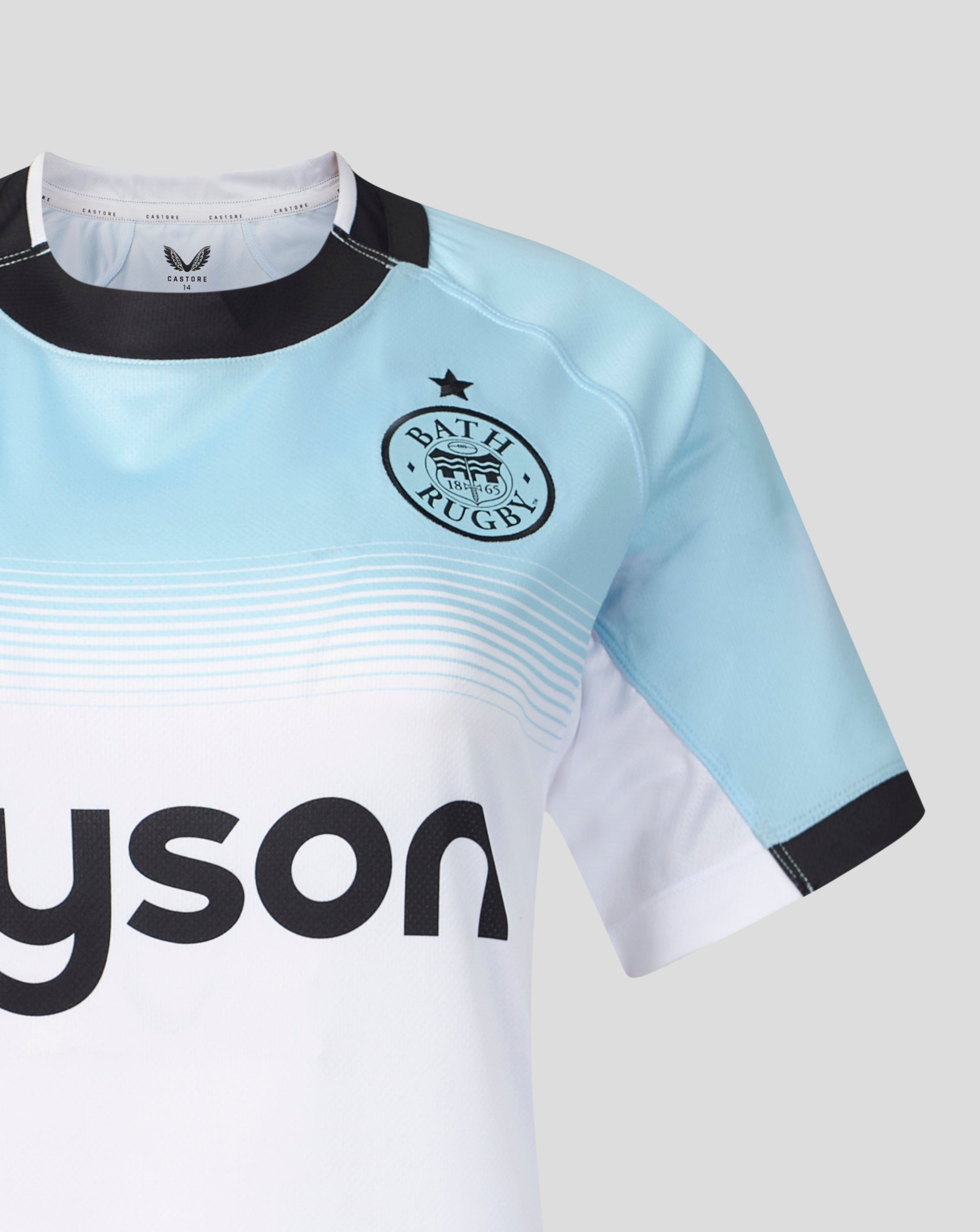 A close-up of a Bath Rugby sports jersey in light blue and white, featuring a black collar, black sleeve cuffs, the Bath Rugby crest on the chest, and a partial black Tyson sponsor logo on the front.