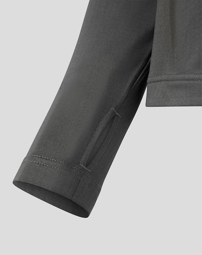 Close-up detail of a dark gray long-sleeve top showing the sleeve cuff with double stitching and a side seam pocket, set against a solid light gray background.