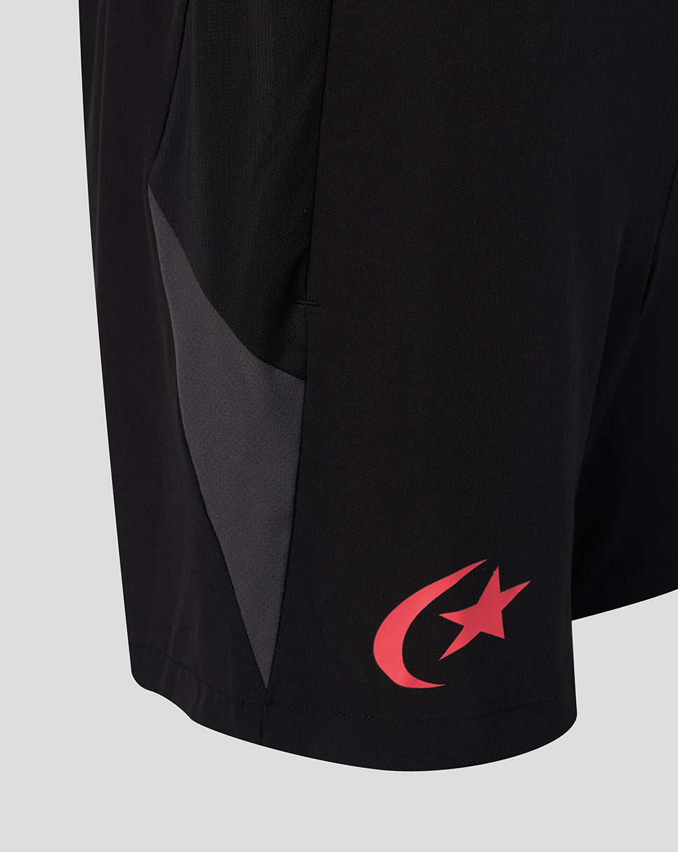 Close-up of black athletic shorts with a dark gray side panel and a red crescent and star logo near the hem, shown on a light gray background.