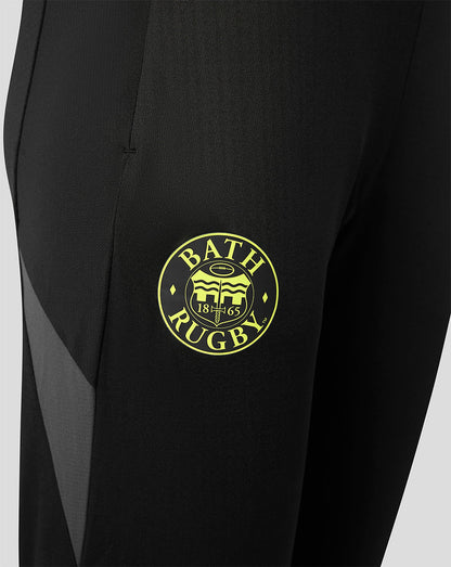 Close-up of a black athletic garment, likely a sports jacket or pants, featuring a circular yellow 'Bath Rugby' crest patch on the chest and a subtle gray side panel.