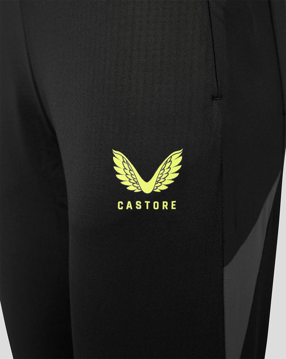 Close-up of black athletic pants featuring a bright yellow winged logo and the brand name 'CASTORE' printed on the thigh.