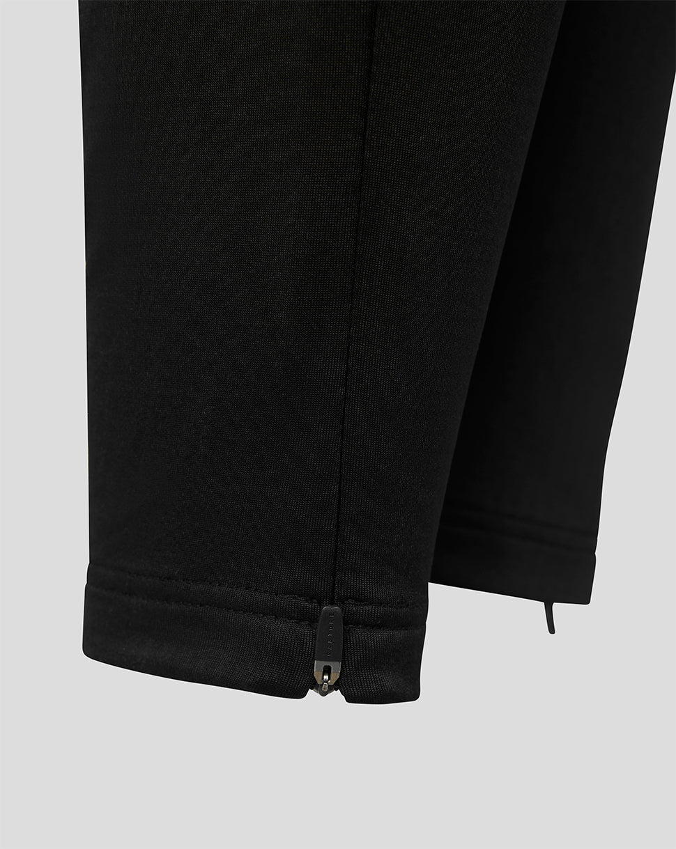 Close-up of black pants showing the hem with a small metal zipper pull tab, on a light gray background.