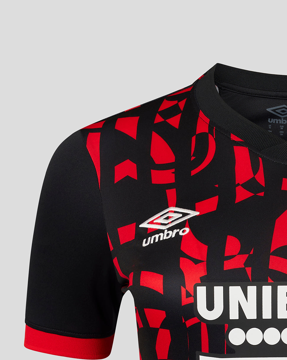 Close-up of a black and red patterned football jersey with white Umbro logos, featuring a geometric abstract print and a red sleeve cuff, shown on a light gray background.