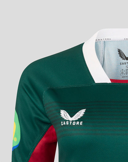 Close-up of a Castore rugby jersey in dark green with a white collar, white chest logo, and red sleeve panel, shown on a light gray background.