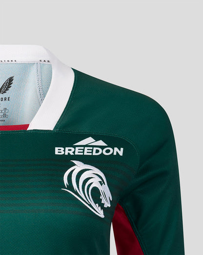 Close-up of a dark green long-sleeve sports jersey with a white collar, white 'BREEDON' text and logo on the chest, and a white animal head graphic below it. A small red panel is visible at the sleeve.