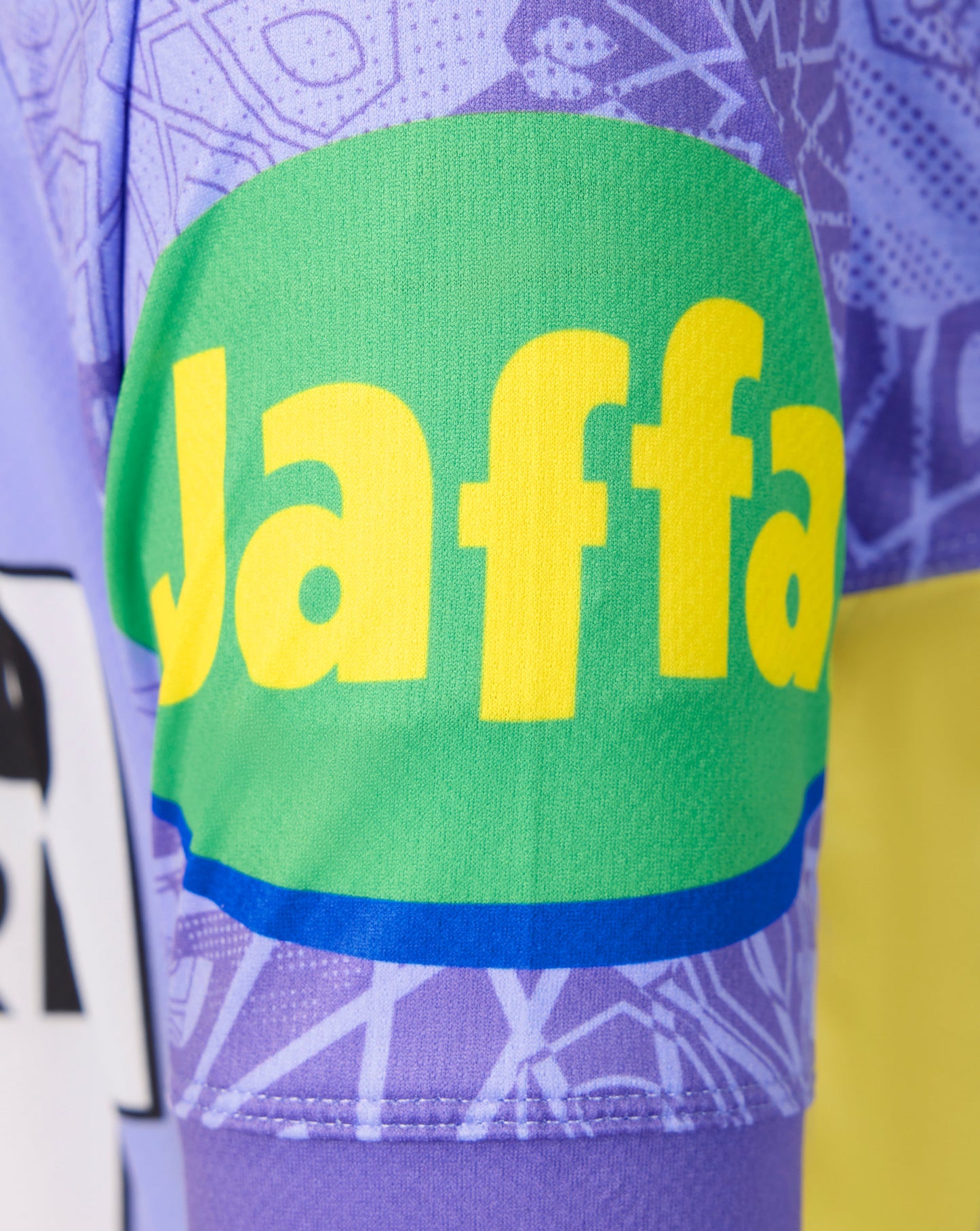 Close-up of a purple patterned athletic jersey with a large green patch on the front featuring yellow 'Jaffa' lettering and a blue stripe.