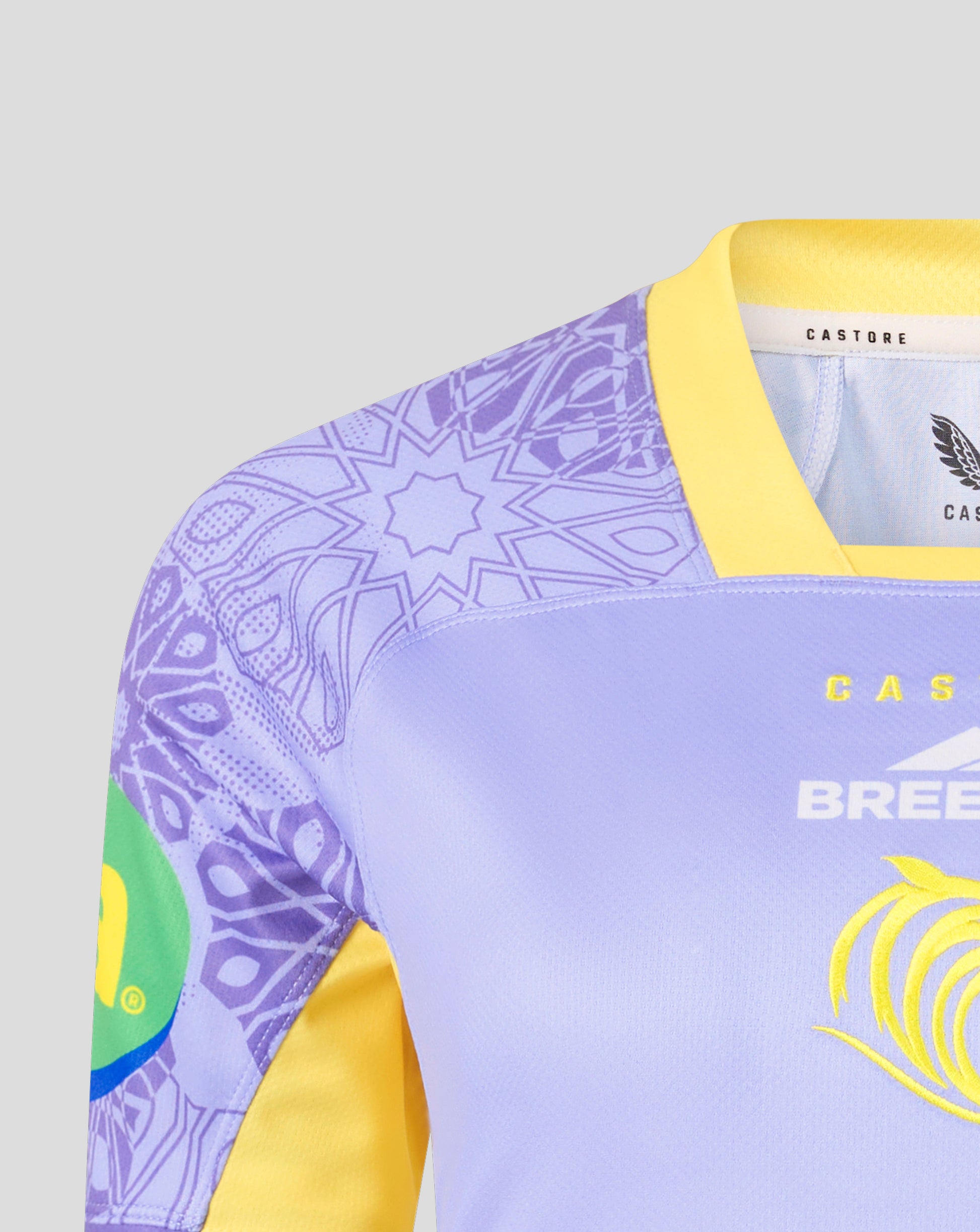 Close-up of a light purple and yellow athletic jersey with a purple mandala pattern on the sleeve, a yellow collar, and yellow branding on the chest.