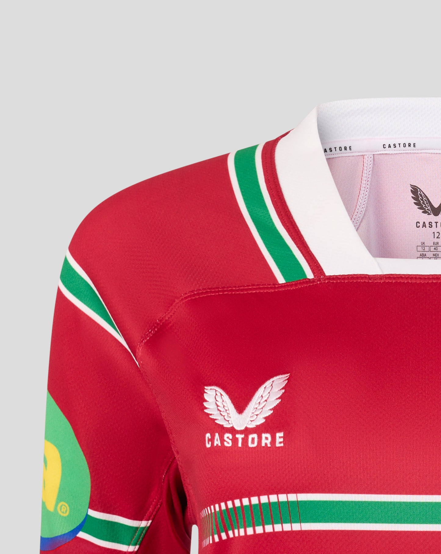 Close-up of a red Castore rugby jersey with green and white stripes, featuring the white Castore wing logo on the chest.
