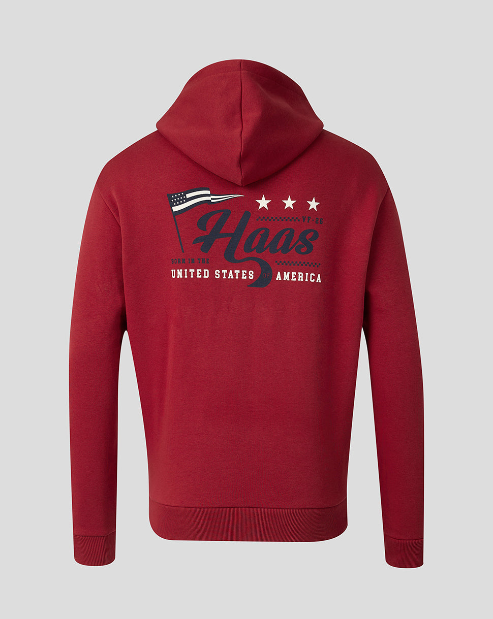 A red pullover hoodie shown from the back, featuring a large graphic print with the word 'Haas' in dark blue script, three white stars, a small American flag, and white text reading 'BORN IN THE UNITED STATES OF AMERICA' on a light gray background.