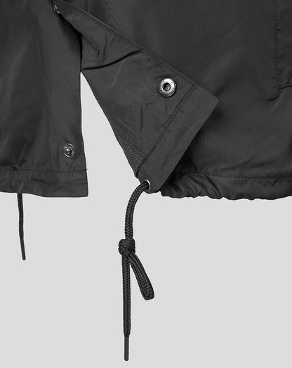 Close-up of a dark gray or black lightweight jacket detail, showing a sleeve cuff with a metal snap button, a drawstring hem, and a knotted black cord against a light gray background.