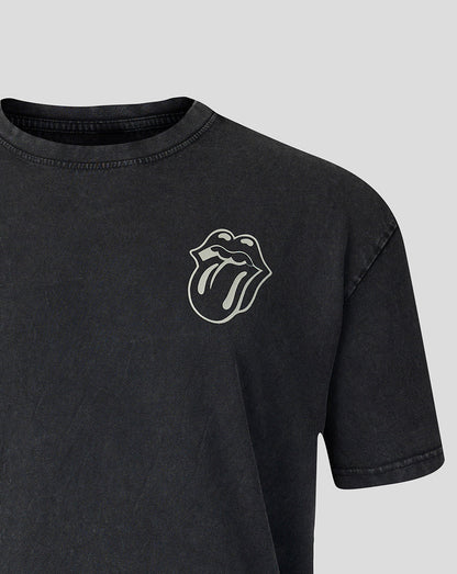 A close-up of a dark gray washed t-shirt featuring the white embroidered Rolling Stones tongue and lips logo on the left chest, set against a solid light gray background.