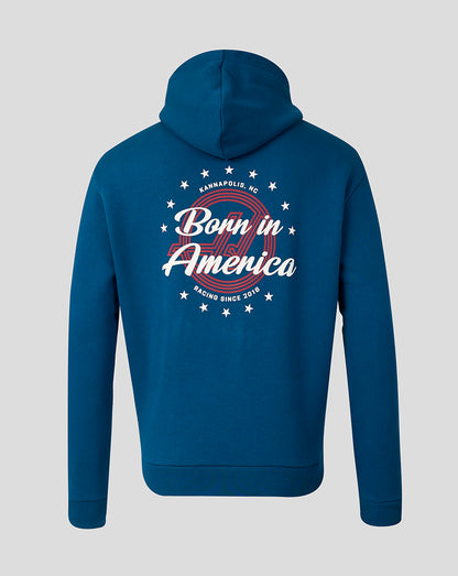 A blue pullover hoodie shown from the back, featuring a large graphic print with the words 'Born in America' in white script over a red circular design, surrounded by white stars and small text reading 'BORN IN AMERICA' and 'RACING SINCE 2017'.