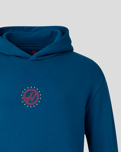 A close-up of a blue hoodie featuring a red and white circular HAAS logo on the centre chest, set against a solid light gray background.