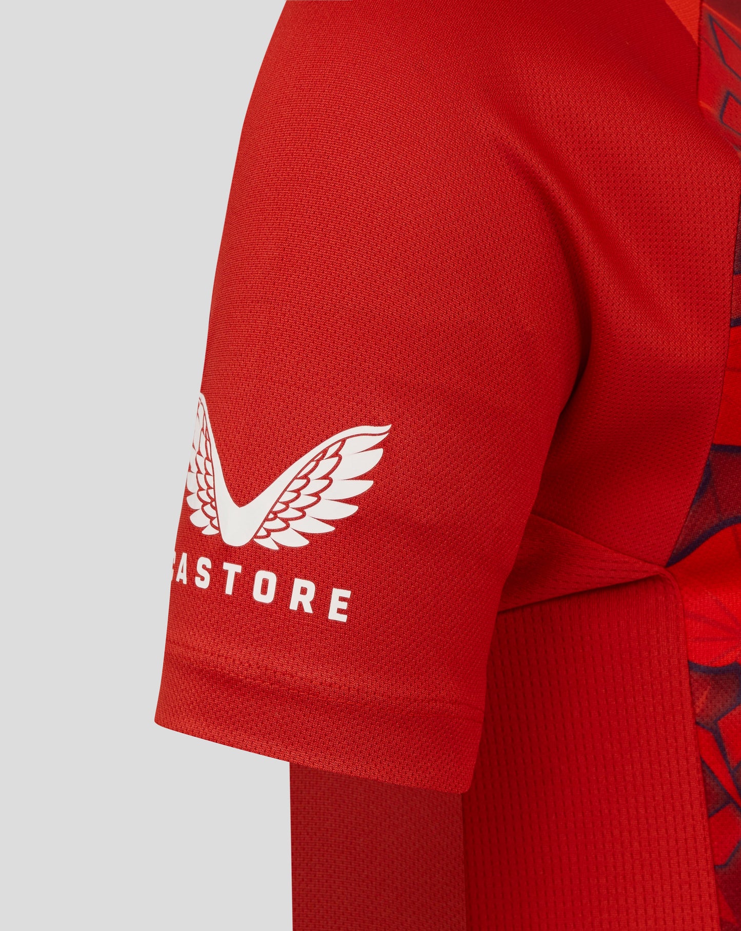 Red sports top with a white Castore logo on the sleeve against a light gray background