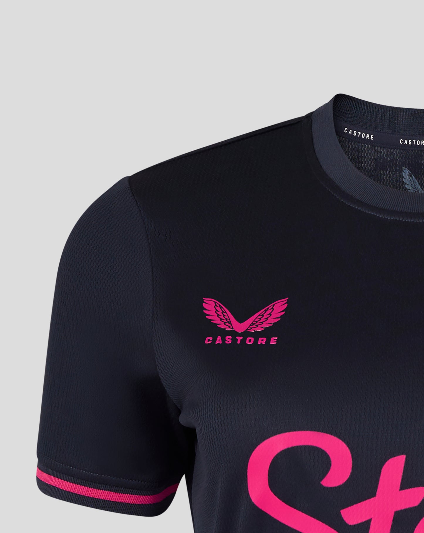Black football jersey with pink accents and 'Castore' logo on a light gray background