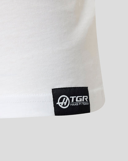 Close-up of a white shirt with a black TGR logo tag on a light gray background