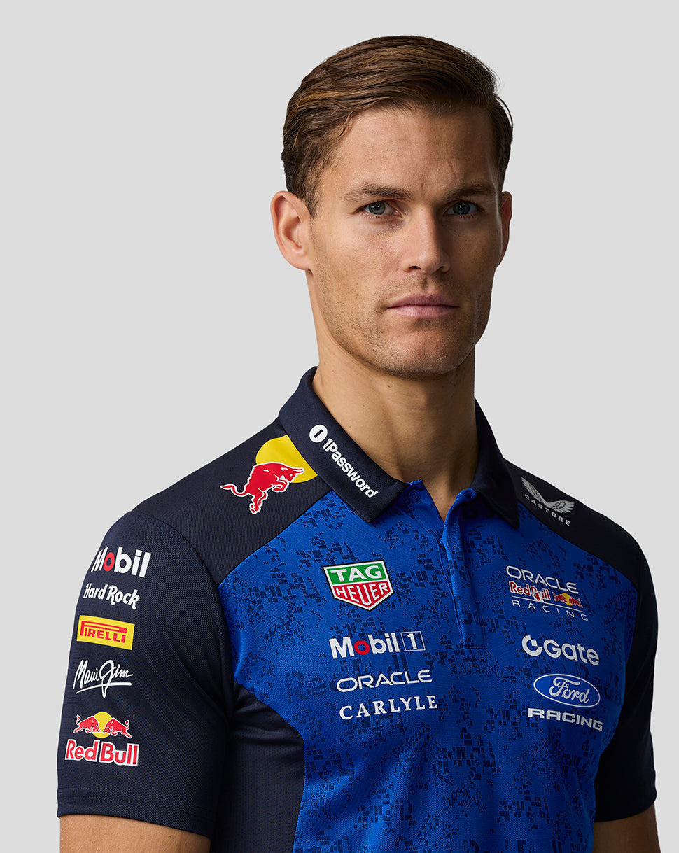 Man wearing a blue racing polo shirt with various sponsor logos on a gray background