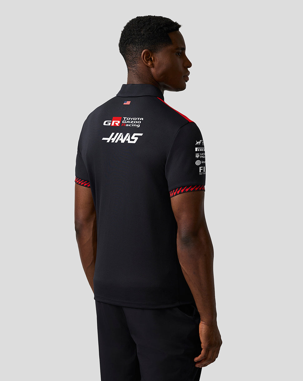 Person wearing a black polo shirt with sponsor logos on a gray background