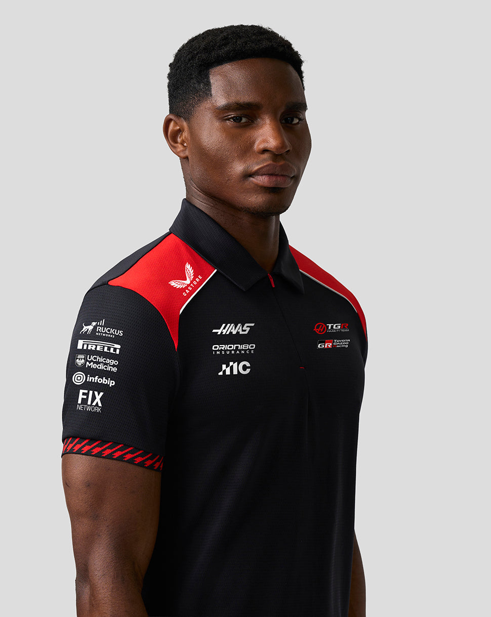 Person wearing a black and red polo shirt with various sponsor logos on a gray background