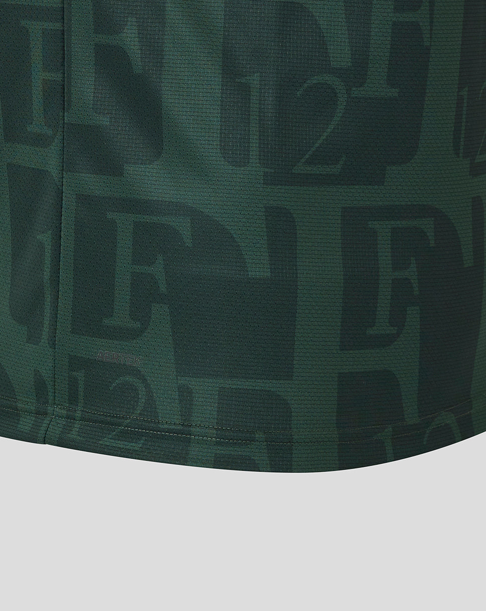 Gold embossed ribbon detail on dark green shirt with subtle crest area at the bottom