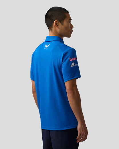 A man shown from the back wearing a bright blue short-sleeve polo shirt with sponsor logos on the back and sleeve, paired with dark navy pants, against a solid light gray background.