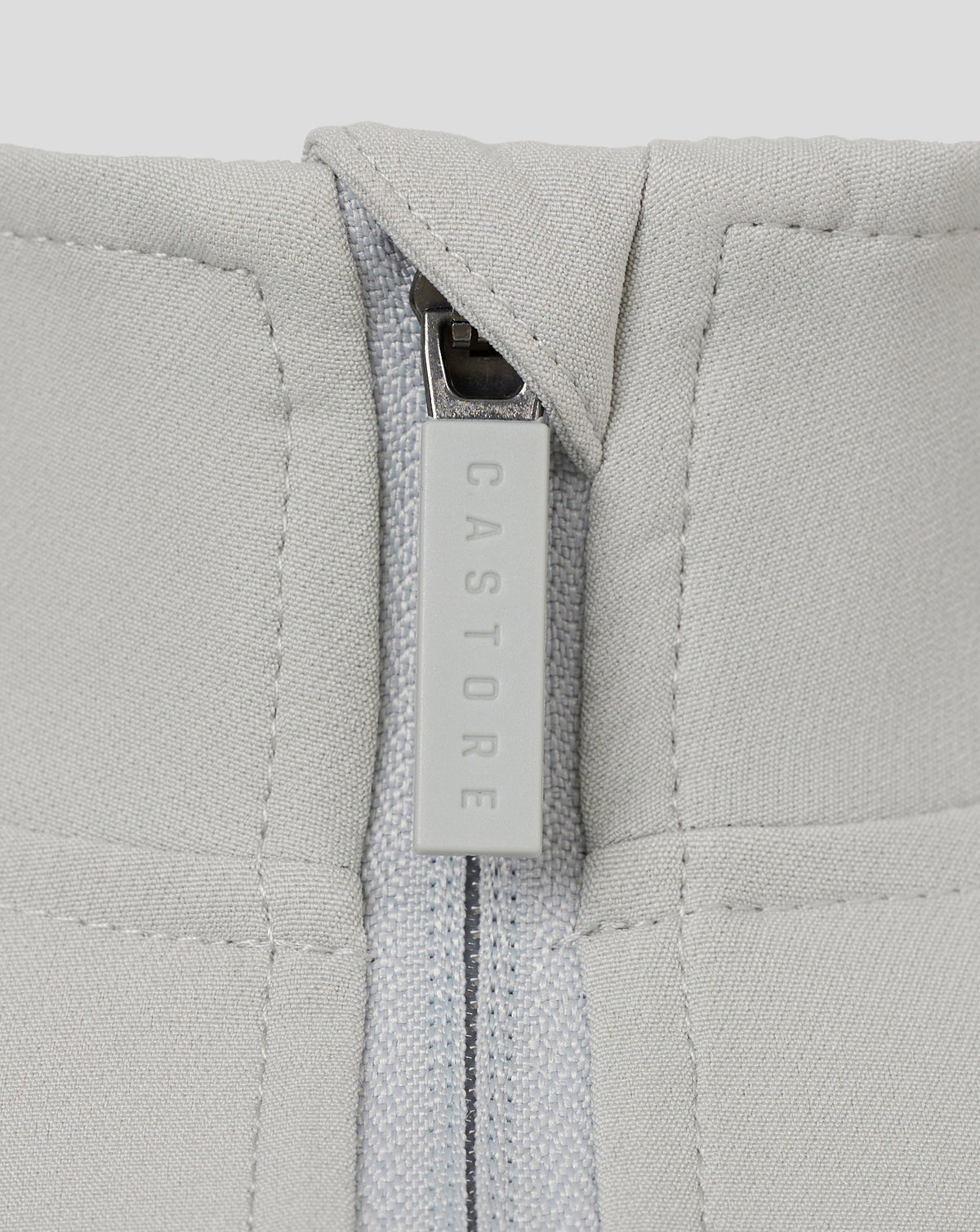 Close-up of light grey track jacket zipper with a CASTORE branded pull.