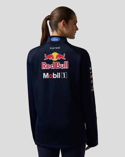 Person wearing a navy jacket with Red Bull and Mobil logos on the back against a light gray background