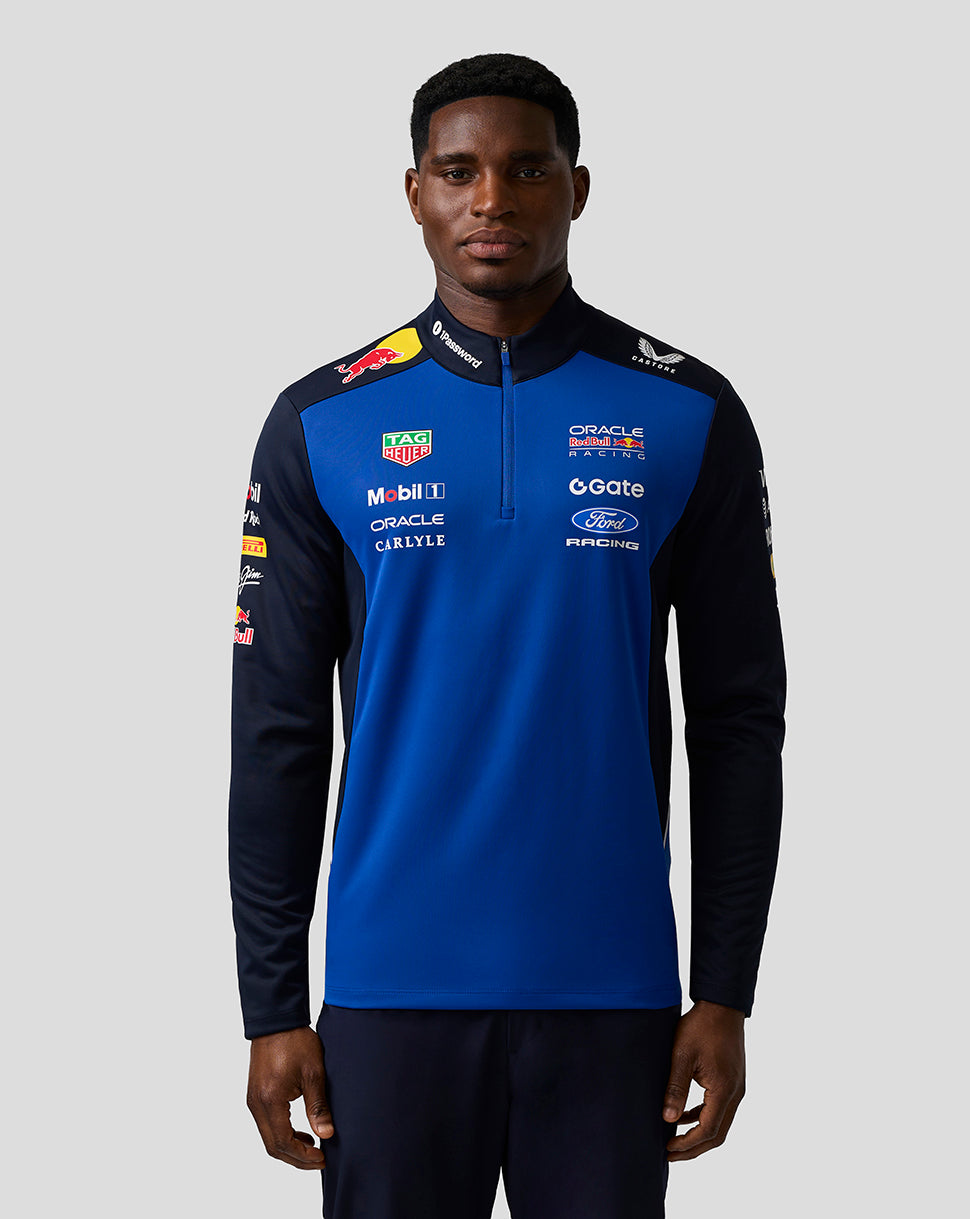 Person wearing a blue and black sports jacket with various sponsor logos on a gray background