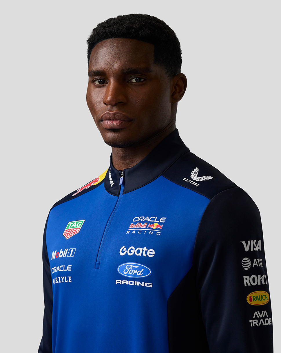 Person wearing a blue racing jacket with various sponsor logos on a gray background