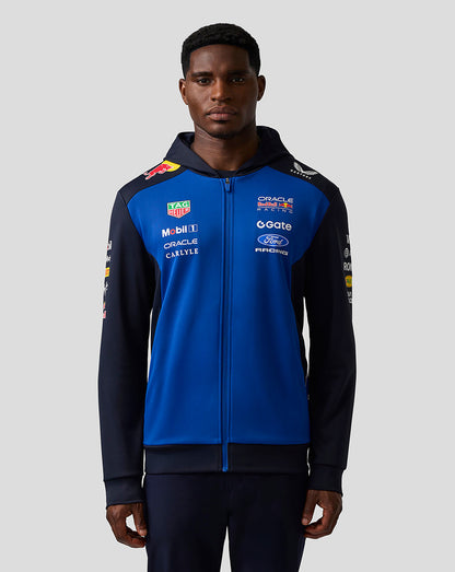 Person wearing a blue and black jacket with various logos on a gray background
