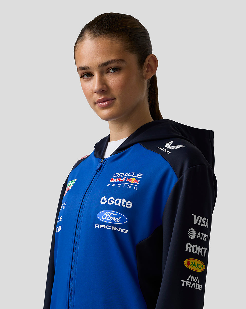 Person wearing a blue and black jacket with various sponsor logos on a gray background