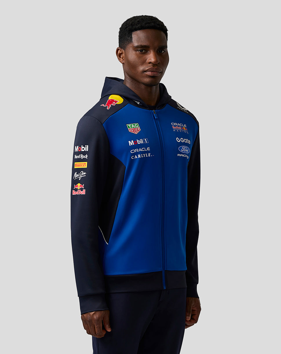 Person wearing a blue and black jacket with various sponsor logos on a gray background