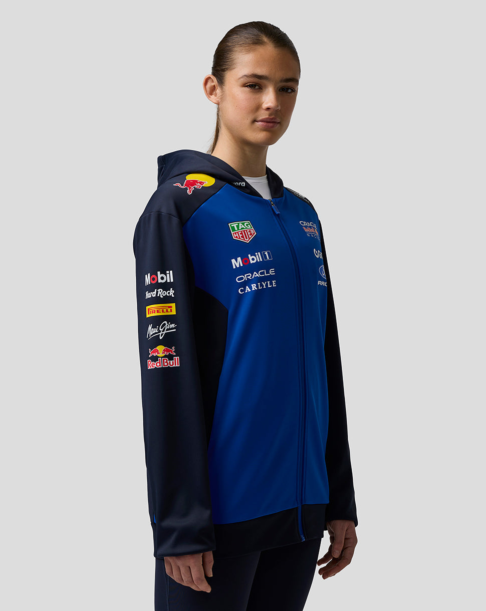 Person wearing a blue jacket with various sponsor logos on a gray background