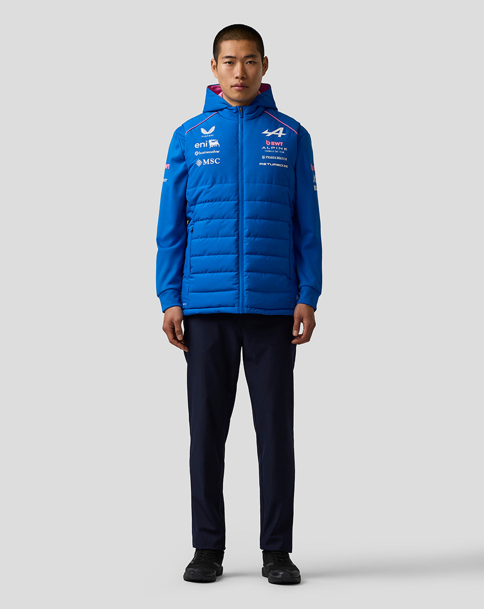 Front three quarter view of a male model wearing a bright blue BWT Alpine Formula One team gilet with chest sponsor logos and front zipper