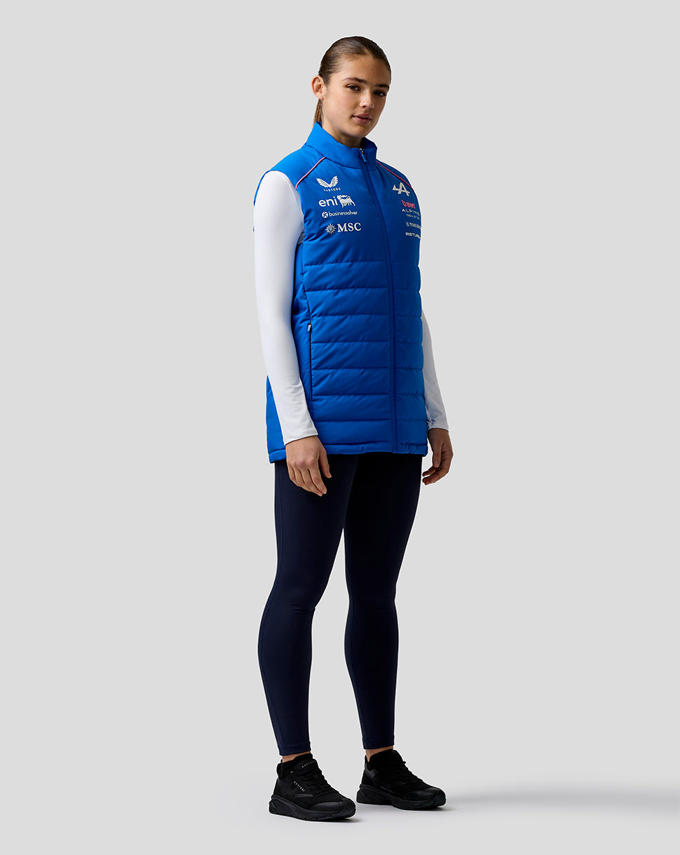 Full length shot of a female model wearing a bright blue BWT Alpine Formula One team gilet over a white long sleeve top showing logos on the chest