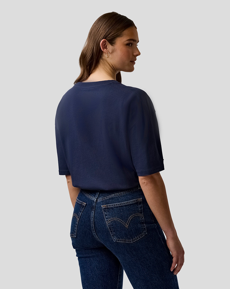 Woman wearing a navy blue t-shirt and dark blue jeans on a light gray background