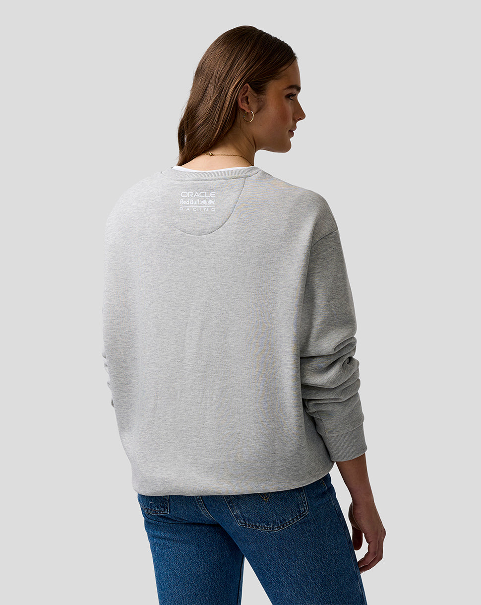 Woman wearing a gray sweatshirt with a logo on the back, standing against a plain background