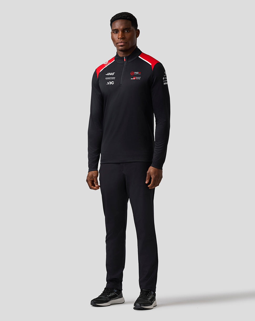 Person wearing a black tracksuit with red accents on a gray background